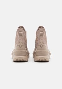 Beige Wildleder-Hochtopsneaker mit dicken Gummisohlen und Stern-Logos auf den Fersenlaschen, von hinten vor einem weißen Hintergrund gezeigt.