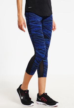 Niebieskie i czarne legginsy capri w wzory z siateczkowymi akcentami, wykonane z elastycznego, oddychającego materiału; w zestawie z czarnymi butami sportowymi.
