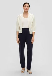 Lichtgewicht, geribbelde crème cardigan met driekwartmouwen, gecombineerd met marineblauwe, rechte broek en neutrale blokhak sandalen.