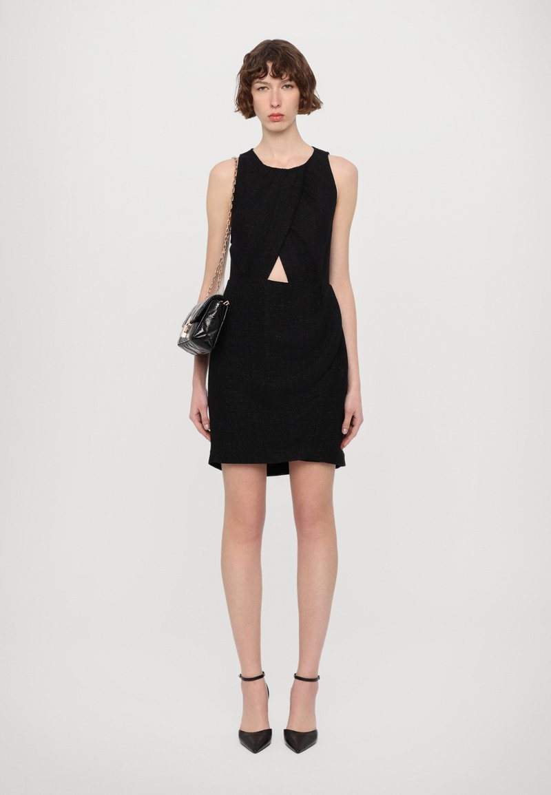 Czarna sukienka bez rękawów z wycięciem w kształcie łezki w talii, teksturowana tkanina i dopasowany krój. Dobrana do małej czarnej torebki.