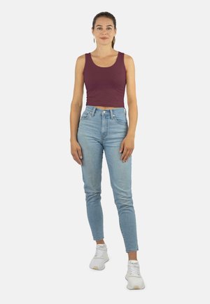 Bordeauxrotes, kurzes Tanktop kombiniert mit hellblauen High-Waist-Jeans. Das Outfit wird durch weiße Sportschuhe ergänzt. Glatter Stoff, figurbetont.