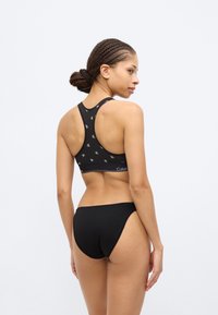 Μαύρο αθλητικό σουτιέν με επαναλαμβανόμενο λογότυπο "CK", σχέδιο racerback και ρυθμιζόμενους ιμάντες, συνδυασμένο με μαύρο μπικίνι χαμηλής μέσης.