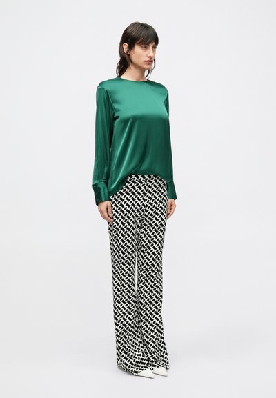 Τοπ από σατέν σε σμαραγδένιο πράσινο με μακριά μανίκια, συνδυασμένο με ψηλόμεσο παντελόνι καμπάνα με μαύρο και άσπρο μοτίβο και λευκά παπούτσια με μυτερή μύτη.