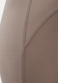 Nahaufnahme von glattem beigem Stoff mit sichtbaren Nähten und Stichen, die geschwungene Linien auf einem Kleidungsstück bilden.