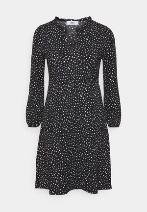 Czarna sukienka do kolan z białymi abstrakcyjnymi kropkami, długimi rękawami, talią zebrana i małym falbankowym dekoltem w kształcie litery V.