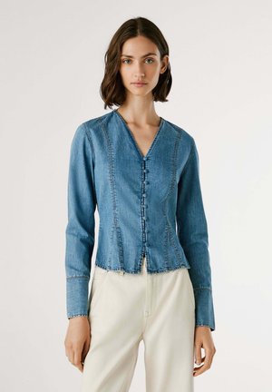 Giacca in denim con scollo a V, maniche lunghe e chiusura a bottoni. Colore azzurro chiaro, con cuciture a vista e orlo sfilacciato.