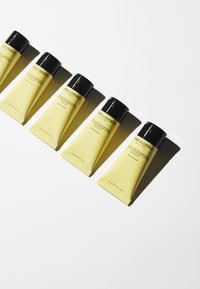 Gula rör med svarta lock i rad, märkta med produktinformation, på en vit bakgrund. Varje rör har SPF 30.