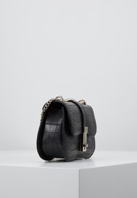 Czarna torebka typu crossbody z ekologicznej skóry o wzorze krokodyla, z srebrowym łańcuszkiem, z klapką oraz prostokątnym kształtem.