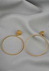 Gold hoop earrings featuring a twisted design, a heart-shaped accent at the clasp, set against a gray textured fabric background.