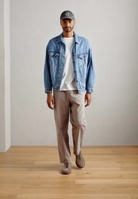 Veste en jean, t-shirt blanc, pantalon beige, casquette grise. La veste a des poches frontales, un col de chemise et un design déboutonné.