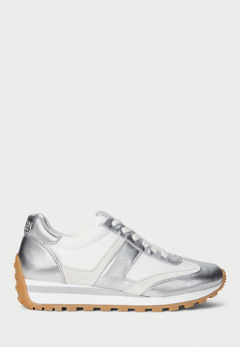 Hopeinen ja valkoinen lenkkari, jossa on teksturoitu päällinen, nauhakiinnitys ja kumipohja. Metalliset yksityiskohdat ja kohotettu kanta.