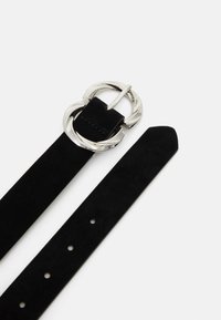 Sort ruskindsbælte med en sølv cirkulær spænde med et snoet design. Stroppen har fem huller til justerbar størrelse.