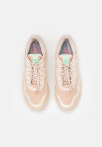 Ljusbeige sportskor med slät yta, tre vita ränder och mintgröna detaljer på tungan. Har en mönstrad innersula.