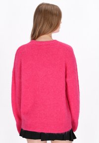 Vaaleanpunainen ylipitkä neulepaita, joka on valmistettu pehmeästä materiaalista; pyöreä kaula-aukko, laskettu olkapäät ja resorit; rento muotoilu, jossa on rispaantunut helma.