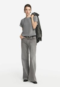 Ljusgrå blus med kort ärm som matchas med bredbeniga grå jeans, accessoriserad med ett svart bälte och en texturerad grå jacka. Svarta skor fulländar looken.