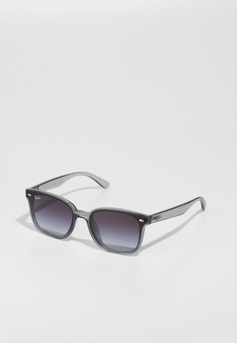 Ochelari de soare gri cu ramă pătrată, lentile întunecate cu gradient și brațe transparente. Prezintă logo-ul Ray-Ban pe tâmplă.