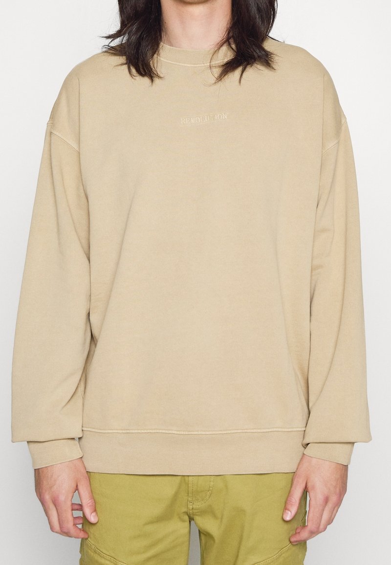 Sudadera de gran tamaño en color beige con cuello y puños acanalados. Presenta un sutil bordado de "REVOLUCIÓN" en el pecho. Tejido suave y casual.