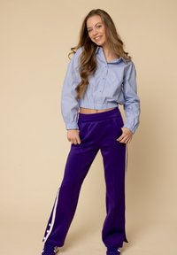 Ingekorte blauw-wit gestreepte shirt met elastische zoom, gecombineerd met paarse broek met witte zijkanten. Glad materiaal, relaxte pasvorm.