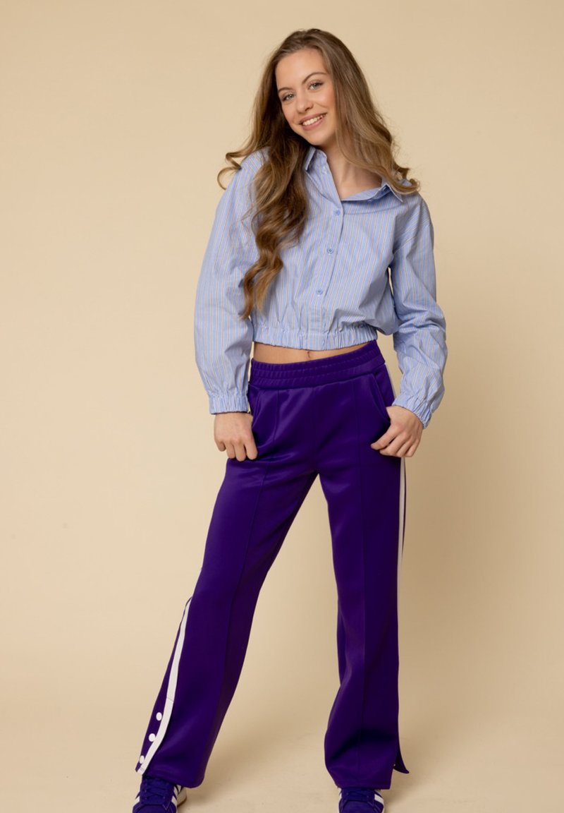 Ingekorte blauw-wit gestreepte shirt met elastische zoom, gecombineerd met paarse broek met witte zijkanten. Glad materiaal, relaxte pasvorm.