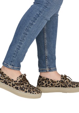 Lower legs wearing blue skinny jeans and leopard print boat shoes with beige soles and brown laces on a white background.