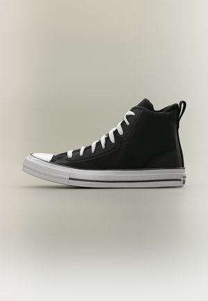 Baskets montantes noires avec lacets blancs, bout renforcé blanc et semelle en caoutchouc blanche sur un fond clair uni.