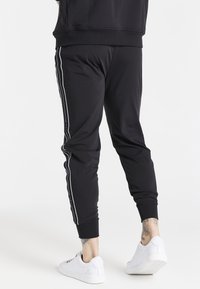 Black jogger pants made of stretchy fabric, featuring white side stripes, elastic cuffs, and a slim fit. Paired with white sneakers.
