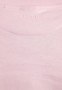 Tissu rose clair avec un logo "HUGO" embossé subtil près du col et des détails de couture visibles sur le dessus.