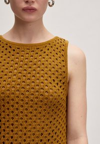Stricktop in Senfgelb ohne Ärmel mit einem offenen, rhombusförmigen Spitzenmuster und einem runden Ausschnitt. Glatte Textur, gerippte Kanten.