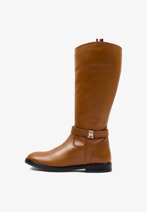 Botte en cuir marron montant jusqu’au genou avec semelle noire basse et sangle décorative avec boucle logo métallique sur le côté.