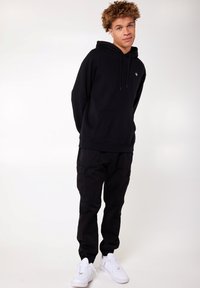 Zwarte hoodie met een voorzak, gecombineerd met zwarte cargobroeken. Witte sneakers maken de outfit af, die een casual, relaxte pasvorm heeft.