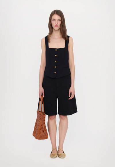 Black sleeveless vest with square neckline and gold buttons, paired with black shorts. Woven orange tote bag and gold flats complete the look.