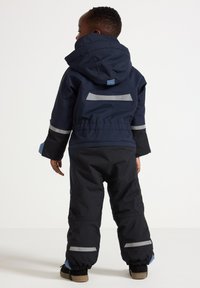 Marineblauwe kinder sneeuwpak met reflecterende accenten, capuchon en elastische manchetten. Verstelbare schouderbanden en een glad, waterdicht materiaal.