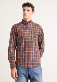 Geruite shirt in rood, groen en geel katoen. Blinde kraag, voorzak en lange mouwen. Gecombineerd met blauwe denim jeans.