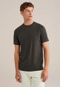 Camiseta de manga corta gris oscuro con cuello redondo, textura suave y corte relajado, combinada con pantalones de color claro.