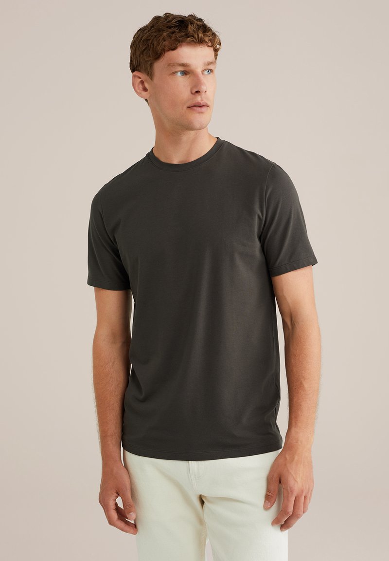 Camiseta de manga corta gris oscuro con cuello redondo, textura suave y corte relajado, combinada con pantalones de color claro.