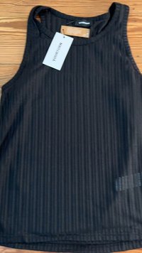 Black ribbed tank top with a round neckline and wide straps. Features a hang tag and subtle logo detail on the fabric.