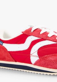 Zapatilla roja con parte superior de cuero liso y acentos de ante, diseño en zigzag blanco y cordones planos blancos. Suela texturizada para mayor agarre.