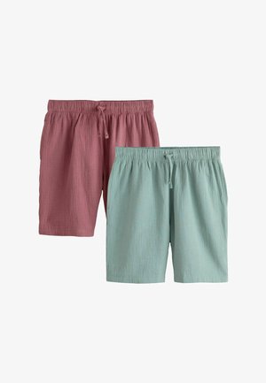 Mann trägt hellgrüne Shorts aus strukturiertem Stoff mit elastischem Bund und Kordelzug, steht mit den Händen in den Taschen vor einem einfarbigen Hintergrund.