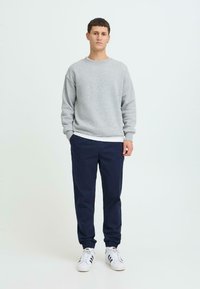 Sweat-shirt gris à col rond associé à un pantalon bleu marine. Le mannequin porte des baskets blanches à rayures noires. Le tissu semble doux et décontracté.