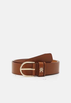 Ceinture en cuir marron avec une boucle en métal doré et un petit logo doré sur la boucle de ceinture, roulée sur un fond blanc.
