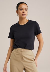 Svart t-shirt med kort ärm, tillverkad av mjuk bomull, med rundad halsringning och en avslappnad passform, kombinerad med beiga högmidjade byxor.