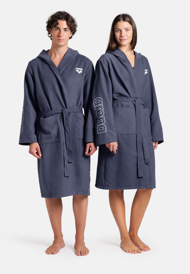 Dvě osoby mají na sobě tmavě šedé koupací pláště s kapucí, které mají strukturovaný vzor a logo "arena" na rukávech. Oba mají boční kapsy.