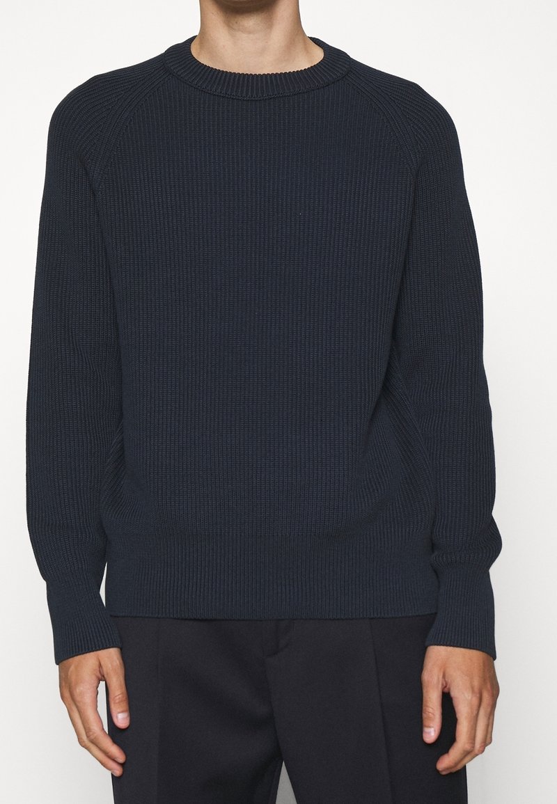 Marinblå ribbade tröja med rund halsringning, långa ärmar och ribbade muddar och nederkant. Tillverkad av texturerat stickat material.