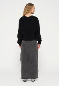 Jersey negro esponjoso con hombros caídos, combinado con una falda larga de denim gris oscuro que presenta bolsillos traseros y costuras visibles.