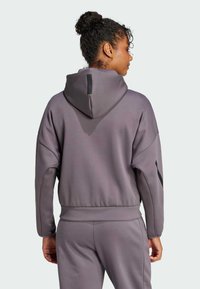 Felpa viola con cappuccio, dal taglio rilassato, polsini e orlo a coste, e dettagli neri sulle maniche. Tessuto testurizzato con una leggera lucentezza.