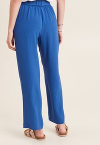 Pantaloni a gamba larga blu, a fantasia, con un elastico in vita, realizzati in un tessuto morbido. Il design presenta una trama delicata e una vestibilità rilassata.
