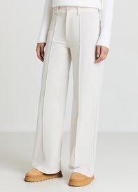 Weit geschnittene Hose aus hellbeigem Rippstoff mit hoher Taille, vorderen Falten und glatter Textur. Kombiniert mit sandfarbenen Schlupfschuhen.