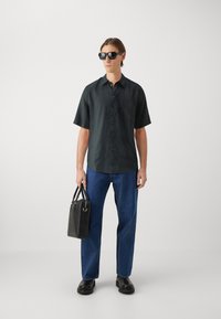 Short-sleeve dark shirt with a button front, paired with blue jeans. Black textured bag and dark sunglasses. Flat shoes complete the look.