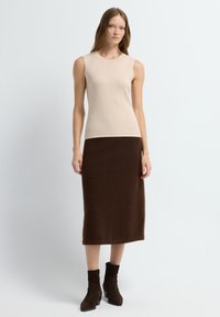 Beige mouwloze top gecombineerd met een bruine, fuzzy brei midi rok. Bruine suède enkellaarsjes met een chunky hak maken de outfit compleet.