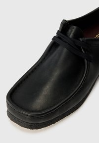 Pantofi din piele neagră cu vârful rotund, suprafață texturată și sireturi negre. Au o talpă din cauciuc și cusături vizibile pe margine.